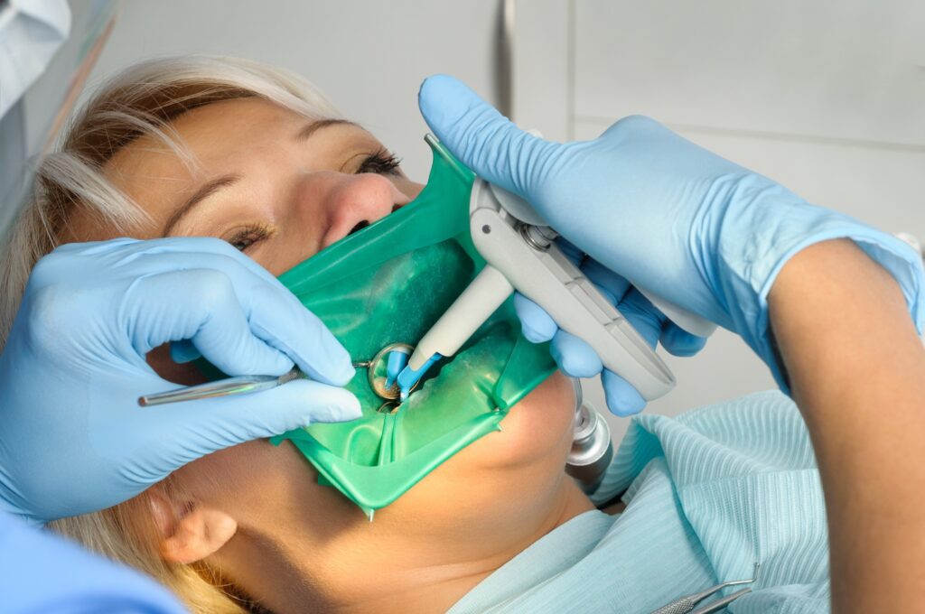 Dentist performing a dental filling procedure on a female patient using curing light and rubber dam